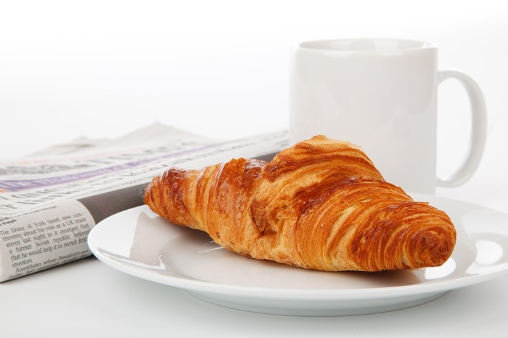 brioche su un piattino con accanto una tazza e un giornale