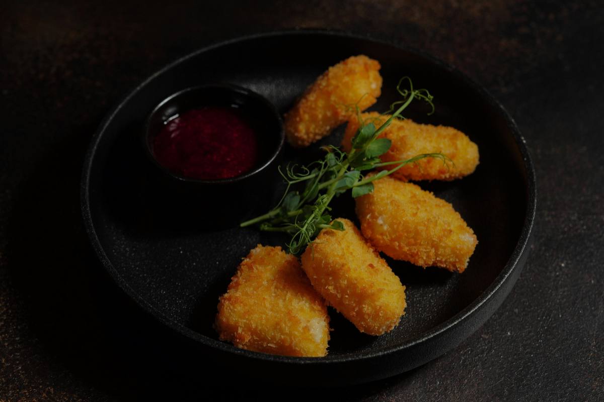 5 nuggets in un piatto nero con accanto una ciotolina con salsa rossa