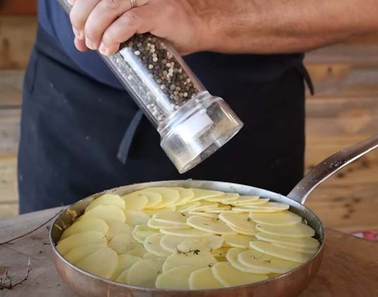 patate tagliate a fetta in padella e una persona che mette pepe col macinino