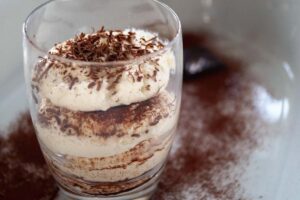 bicchiere pieno di tiramisù sopra un piatto spolverato di cacao