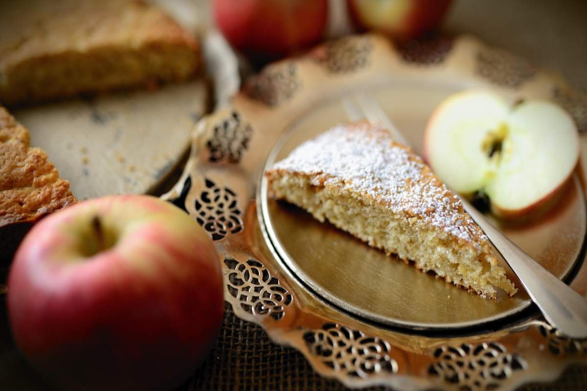 fetta di torta su un piatto con accanto una forchettina e delle mele