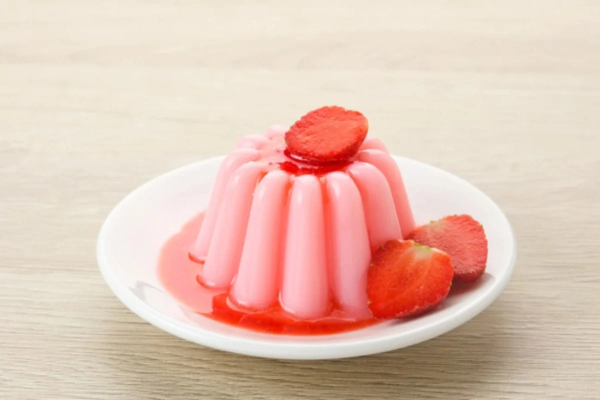 budino alle fragole su un piatto con accanto fragole fresche e sotto una salsa alle fragole