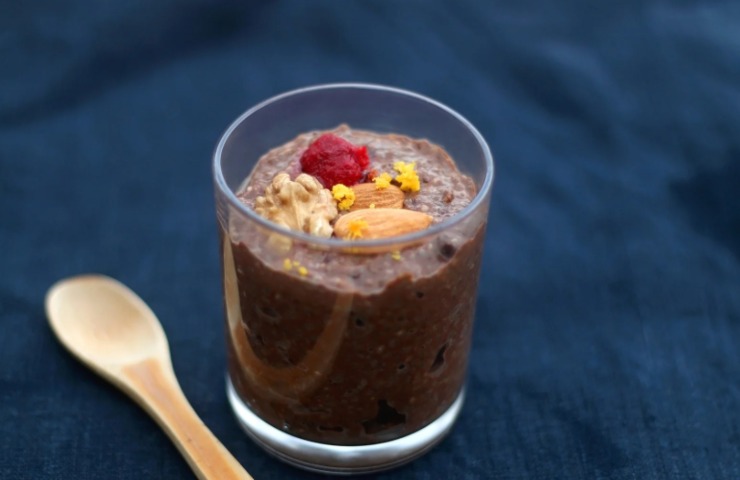 budino al cacao dentro ad un bicchiere di vetro con sopra frutta fresca a frutta secca e accanto un cucchiaino