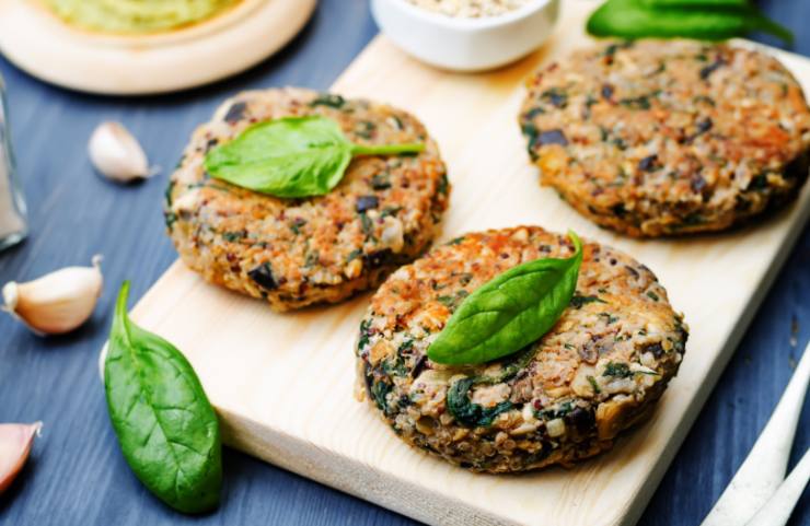 tre burger sopra ad un tagliere con sopra delle foglie di basilico