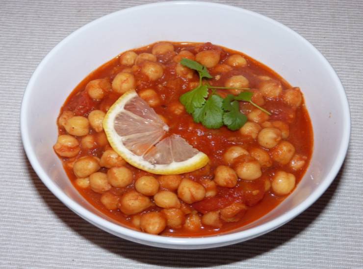 ceci al pomodoro dentro ad un piatto con sopra una fettina di limone e una foglia di coriandolo