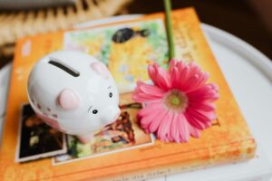 salvadanaio sopra ad un libro con accanto un fiore rosa