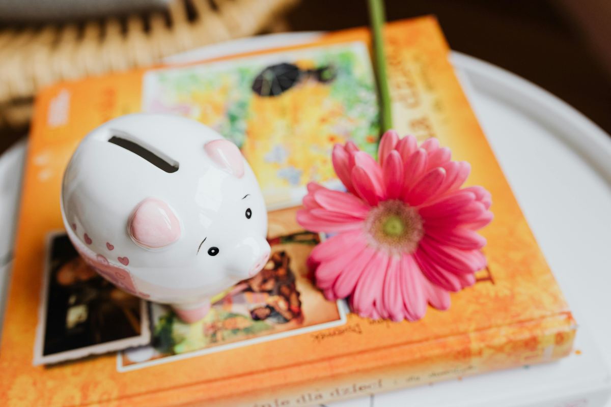 salvadanaio sopra ad un libro con accanto un fiore rosa