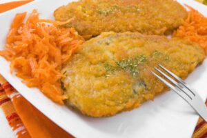 due cotolette in un piatto con accanto delle carote e una forchetta