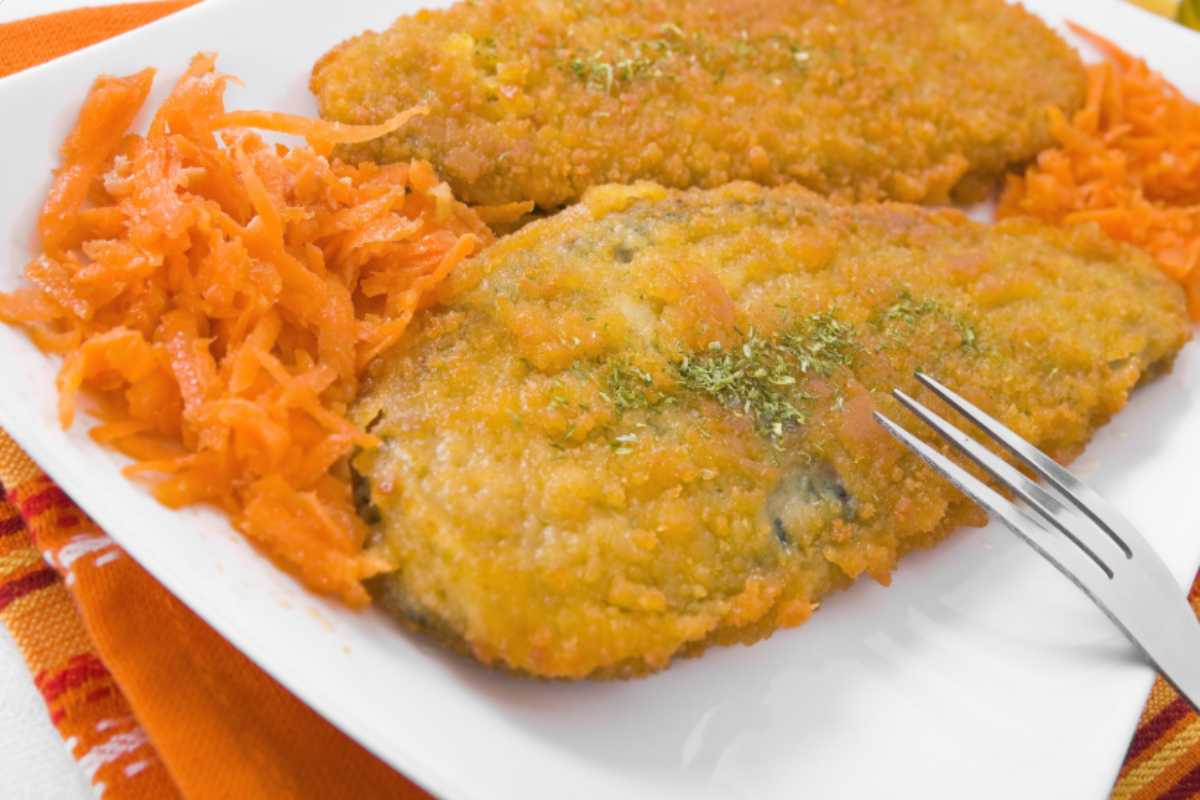 due cotolette in un piatto con accanto delle carote e una forchetta