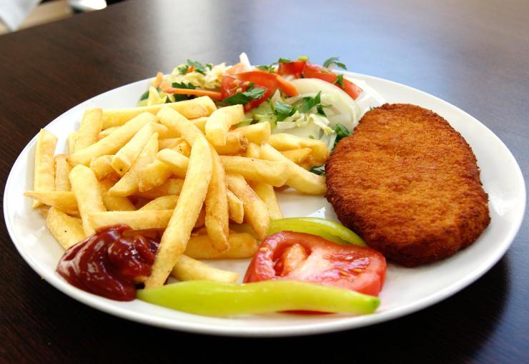 cotoletta su un piatto con accanto patatine fritte, pomodoro, insalata e ketchup