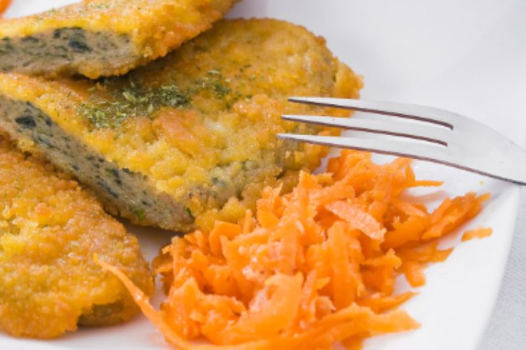 cotoletta tagliata dentro al piatto con accanto delle carote e una forchetta