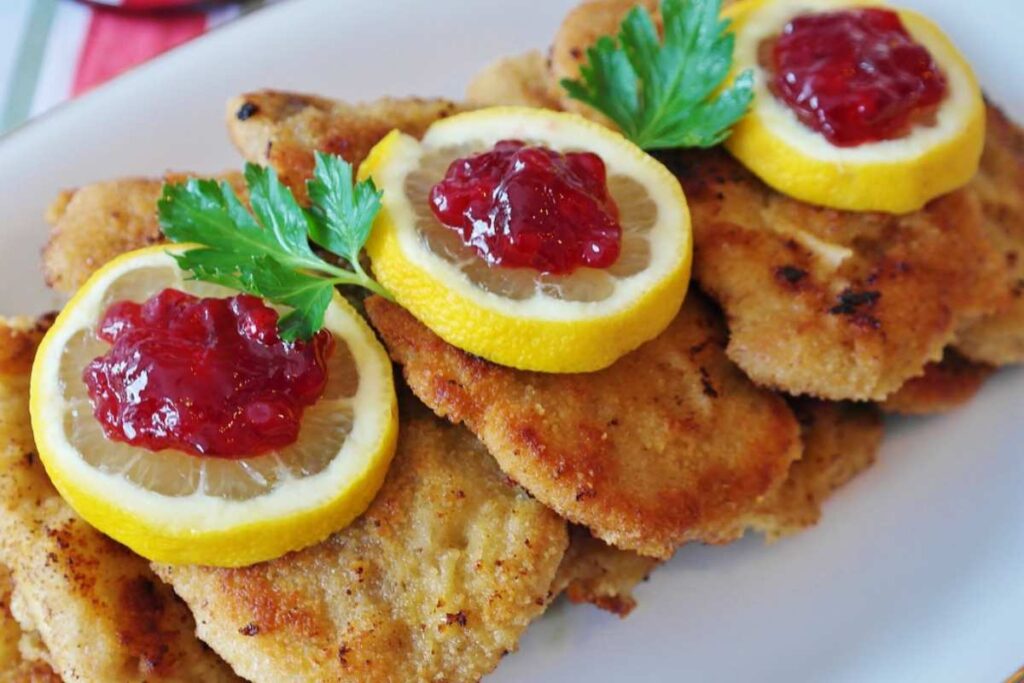 cotolette su un piatto con sopra delle fettine di limone e una salsina rossa