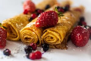 tre crepes arrotolate su un piatto con accanto delle fragole