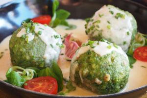 tre gnocchi di spinaci dentro ad un piatto con una salsa bianca, delle foglie di spinaci e dei pomodorini