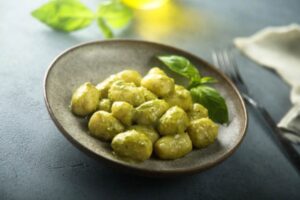 gnocchi al pesto dentro ad un piatto con sopra due foglioline di basilico