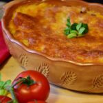 teglia di lasagne con accanto dei pomodori
