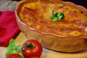teglia di lasagne con accanto dei pomodori