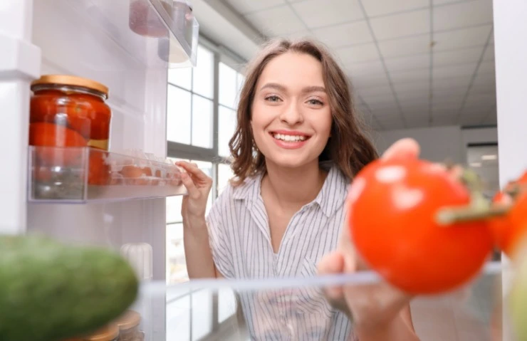 donna sorridente che prende un pomodoro dal frigo