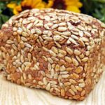 pane bauletto ricoperto di semi sopra ad un tagliere di legno e dietro dei girasoli