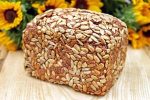 pane bauletto ricoperto di semi sopra ad un tagliere di legno e dietro dei girasoli