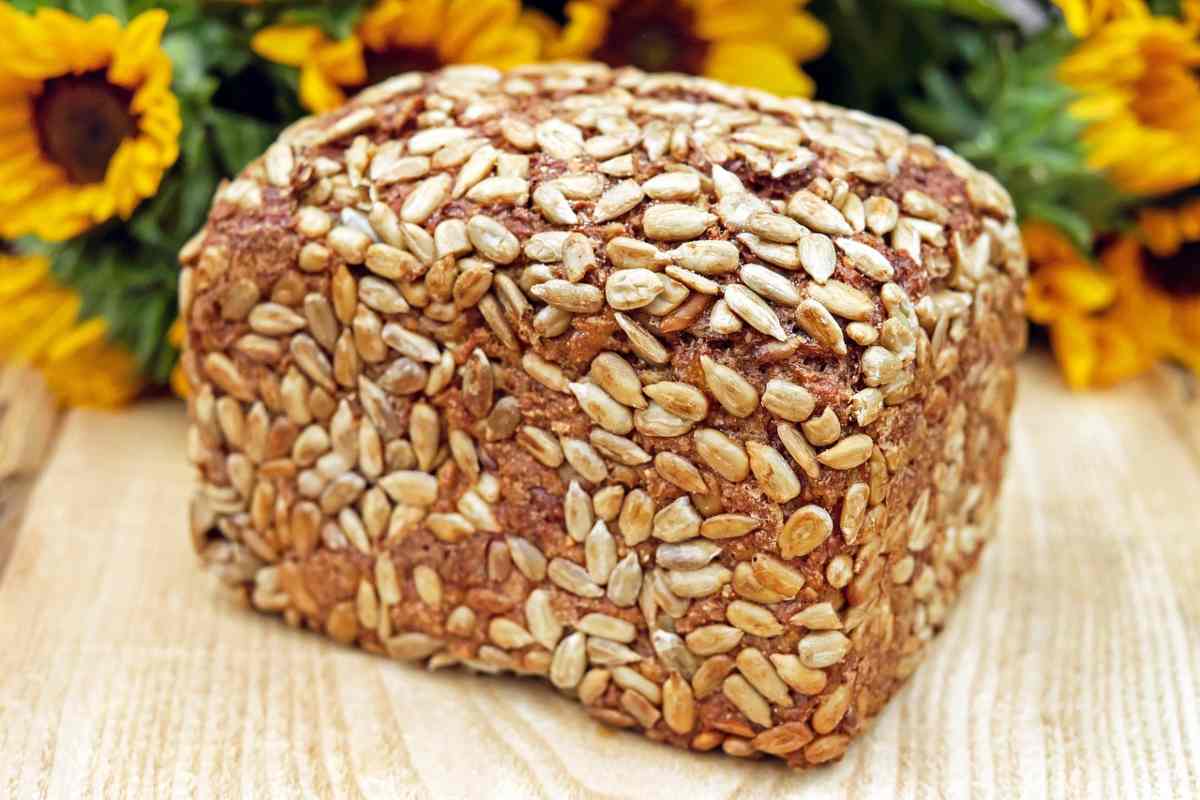 pane bauletto ricoperto di semi sopra ad un tagliere di legno e dietro dei girasoli