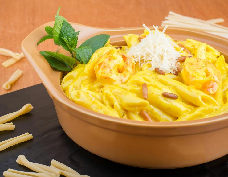 teglia di pasta condita con una salsa gialla e foglie di basilico