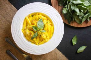 piatto di pasta con una salsa gialla e sopra qualche foglia di basilico con accanto del basilico