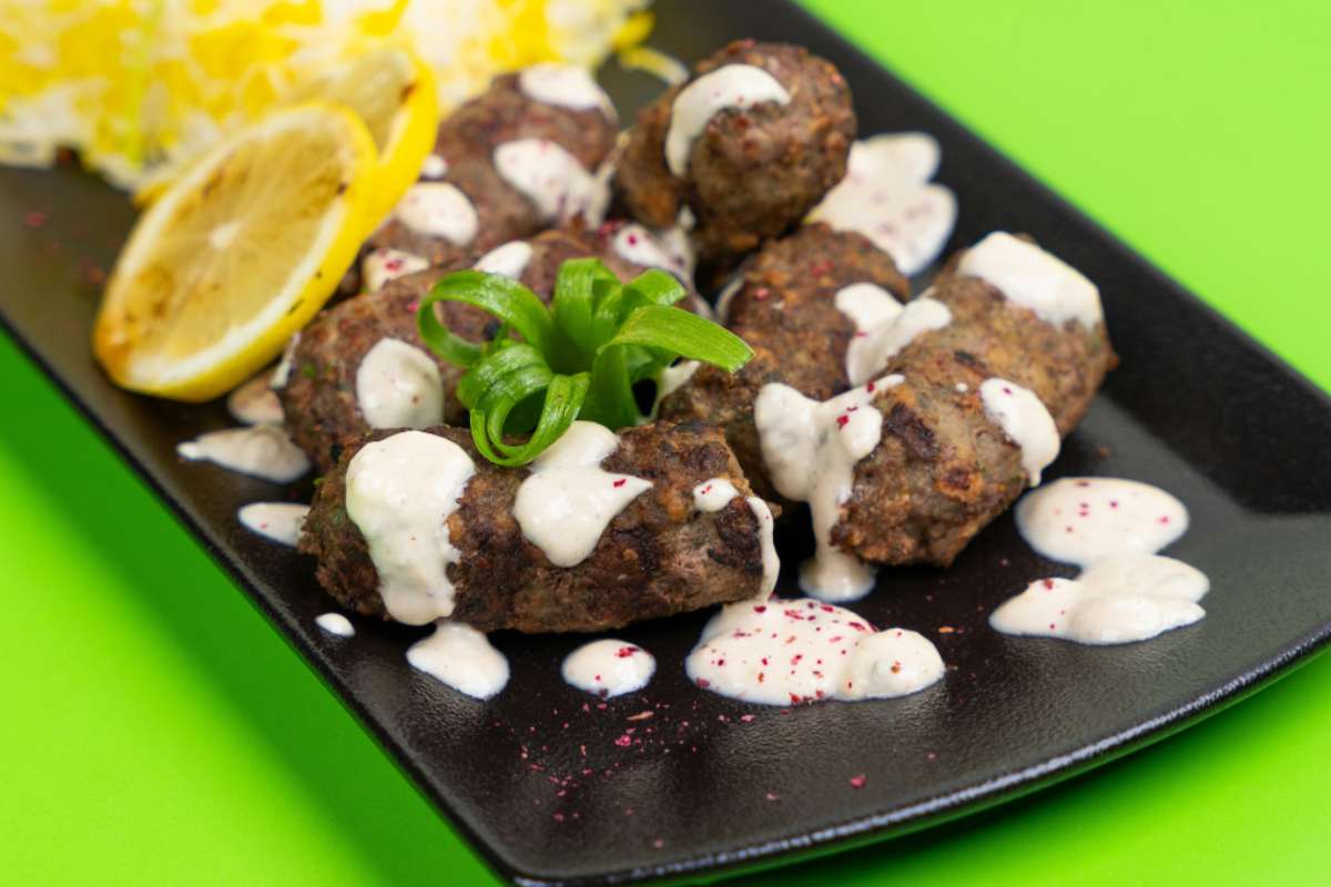 polpette su un piatto nero ricoperte da una salsina bianca con accanto una fettina di limone