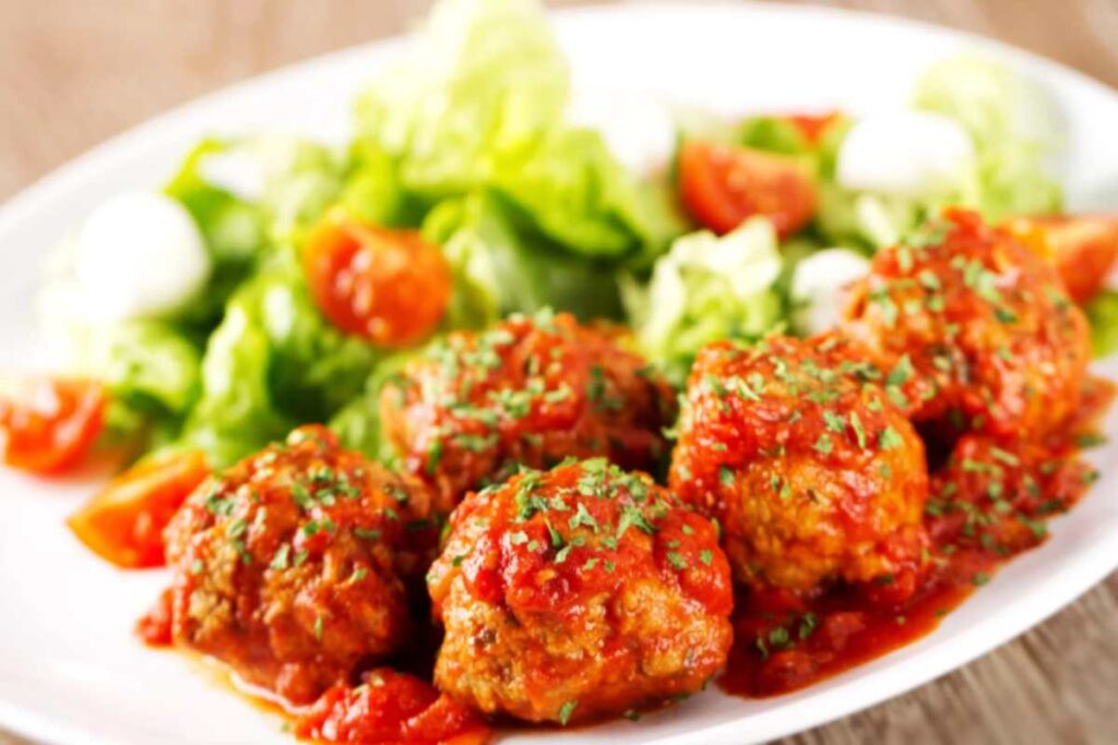 polpette al sugo in un piatto con accanto insalata e pomodori
