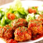 polpette al sugo in un piatto con accanto insalata e pomodori