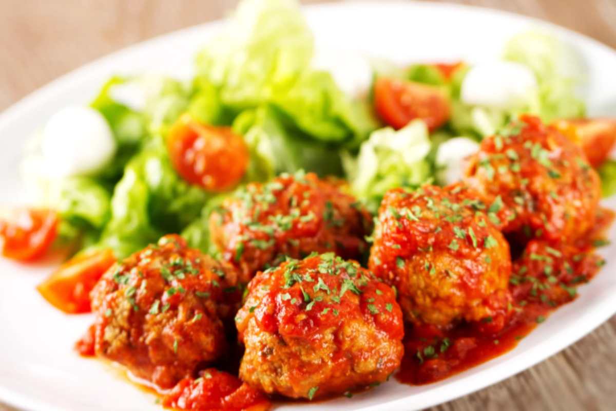 polpette al sugo in un piatto con accanto insalata e pomodori