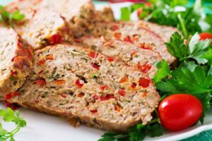 fette di polpettone sopra ad un piatto con accanto insalata e pomodori
