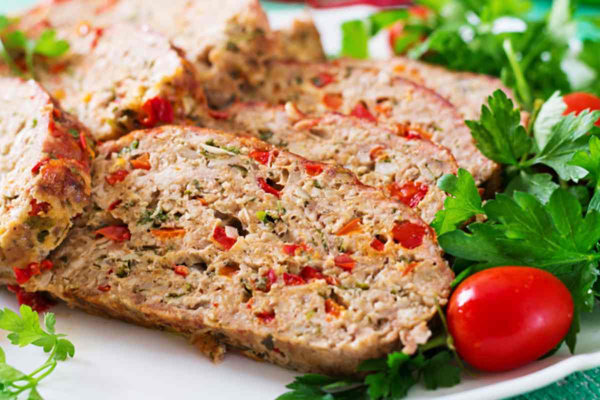 fette di polpettone sopra ad un piatto con accanto insalata e pomodori