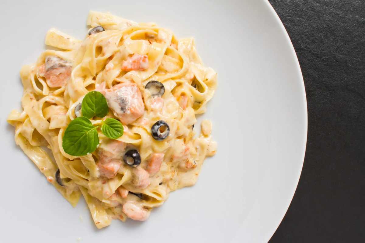 Piatto di pasta con salmone, olive nere e basilico