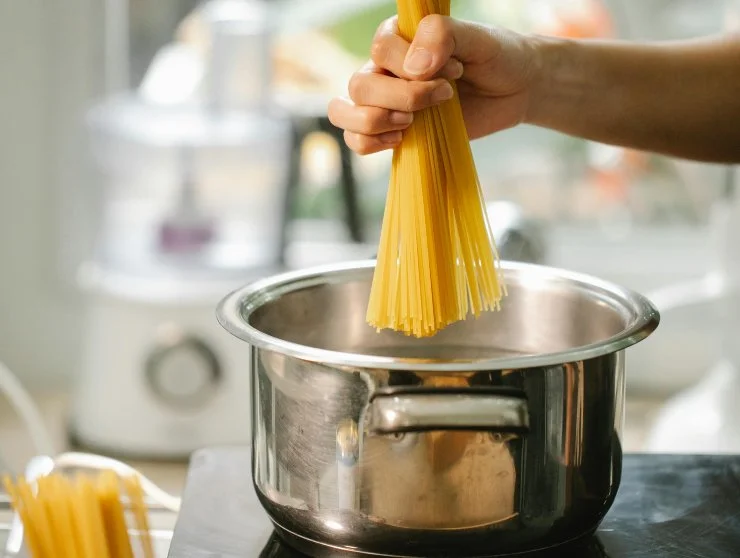 persona che cala gli spaghetti dentro alla pentola sul fornello