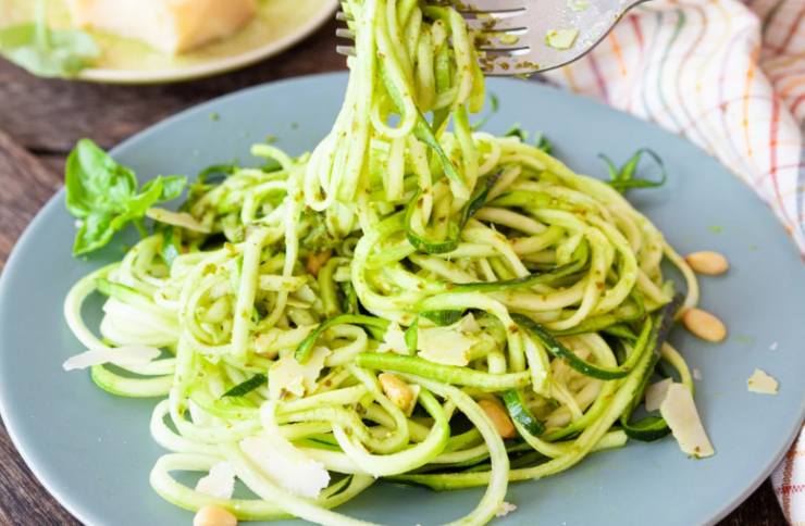 persona che prende con la forchetta degli spaghetti di zucchine al pesto