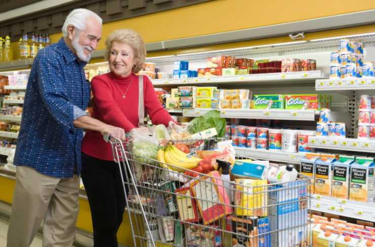 uomo e donna anziani al supermercato con un carrello pieno di cibo
