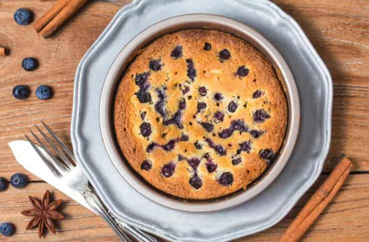 torta di mirtilli dentro ad una tortiera e accanto delle stecche di cannella