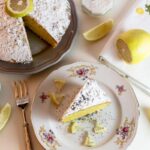 torta al limone con accanto dei limoni e un piattino con sopra una fetta della medesima torta