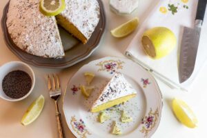 torta al limone con accanto dei limoni e un piattino con sopra una fetta della medesima torta