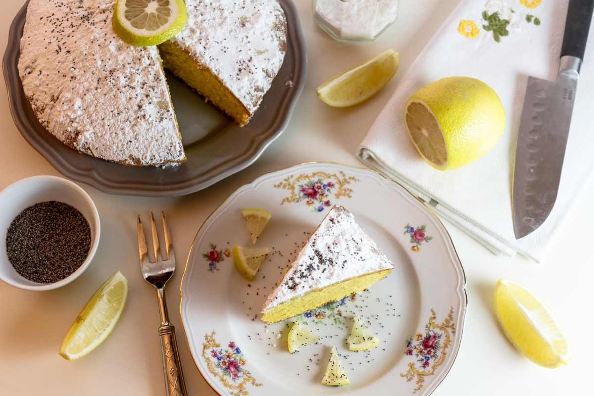 torta al limone con accanto dei limoni e un piattino con sopra una fetta della medesima torta