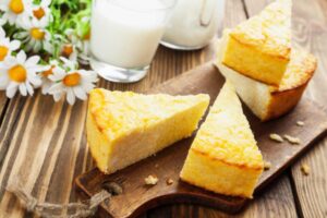 tre fette di torta su un tagliere con accanto delle margherite e dei bicchieri di latte