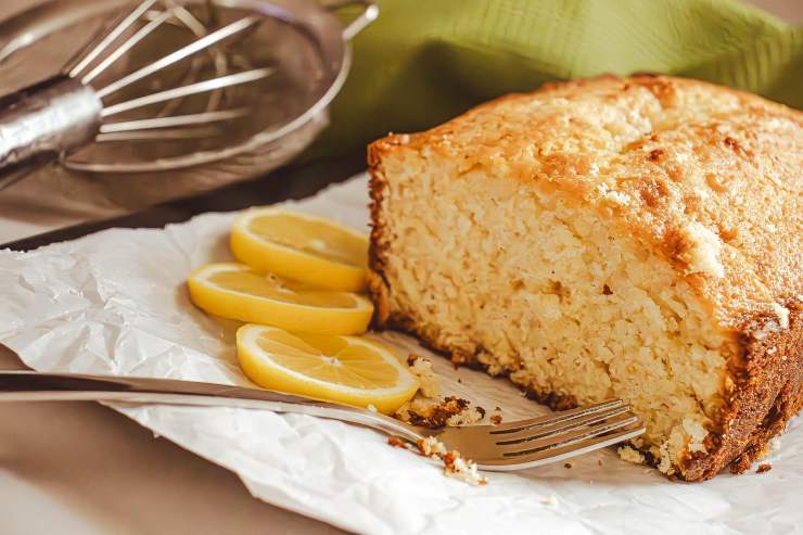 mezzo plumcake su un piatto con accanto delle fette di limone e una frusta da cucina