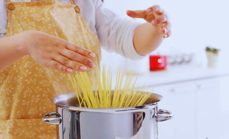 mani mettono la pasta in acqua bollente