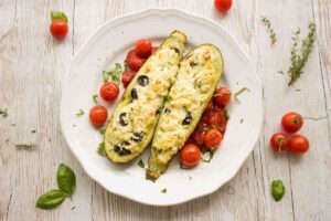 due zucchine ripiene su un piatto con accanto dei pomodorini