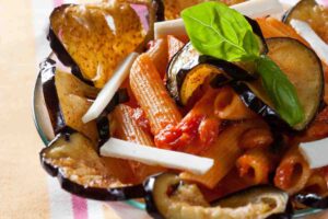 coppa con melanzane fritte sui bordi e al centro pasta al pomodoro guarnita con scaglie di ricotta salata e foglie di basilico per ricette estive sfiziose