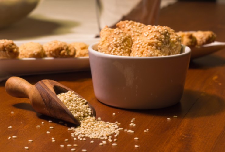 biscotti dentro ad un contenitore e accanto un mestolo con dei semi di sesamo