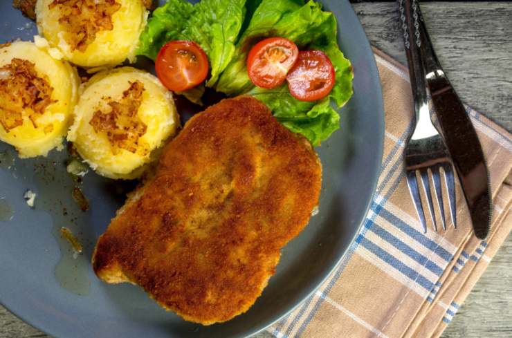 cordon bleu in un piatto con patate insalata e pomodori e accanto le posate