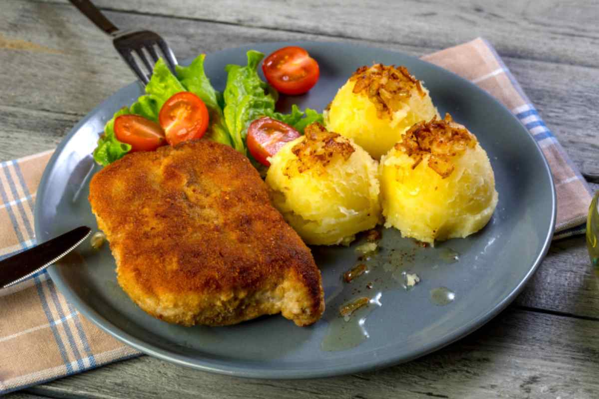 cordon bleu su un piatto con accanto patate, insalata e pomodori