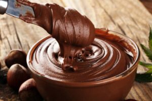 ciotola di vetro piena di crema spalmabile al cacao con intorno delle nocciole